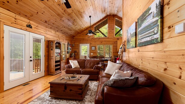 A cozy cabin interior with a wooden ceiling, a leather sofa, a coffee table, and a painting of a car on the wall. - Cabin Blue Ridge-Murphy area, fast wifi, dog & family friendly, trail & hot tub! (Murphy)