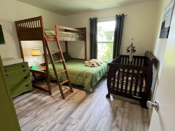Ein Zimmer mit Etagenbett, Babybett, einer Himmelsleiter, einem Schminktisch und einem Fenster mit Vorhängen.