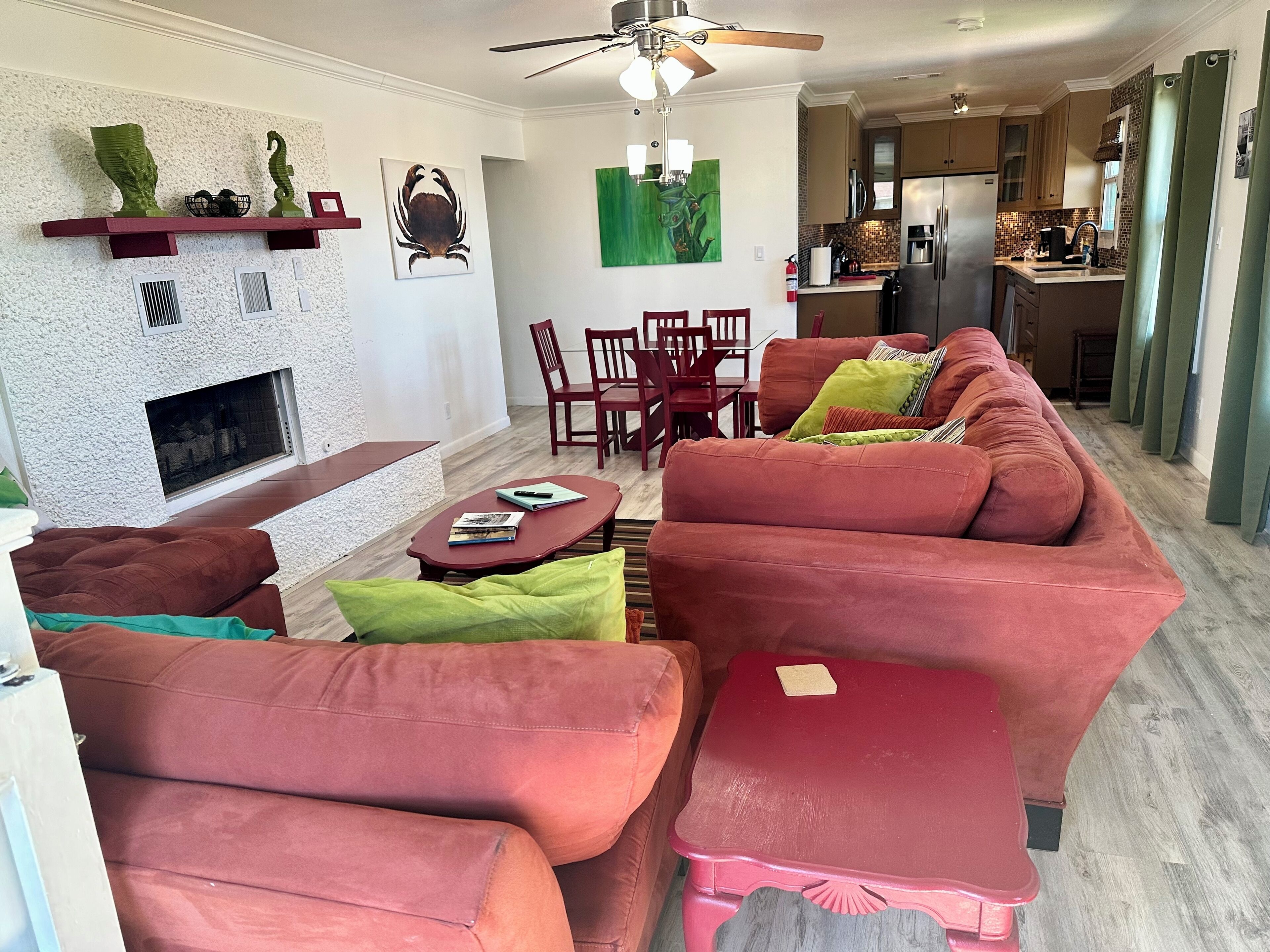 A living room with a fireplace, red sofas, a dining area with chairs, and a kitchen in the background.