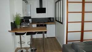 Een compacte keuken met een houten aanrecht, een spoelbak, een magnetron, een koffiezetapparaat en een vaatwasser. Er staan twee barkrukken bij het aanrecht.