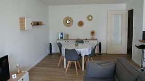 Een moderne woonkamer met een eethoek, met een ronde tafel, grijze stoelen, een grijze bank en een houten vloer.