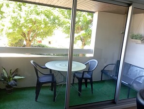 Un balcon avec une table ronde et deux chaises, un pot de fleurs et une vue sur les arbres et les bâtiments.