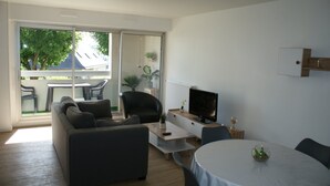 Een moderne woonkamer met een bank, een televisie, een eettafel en een balkon met buitenmeubilair.