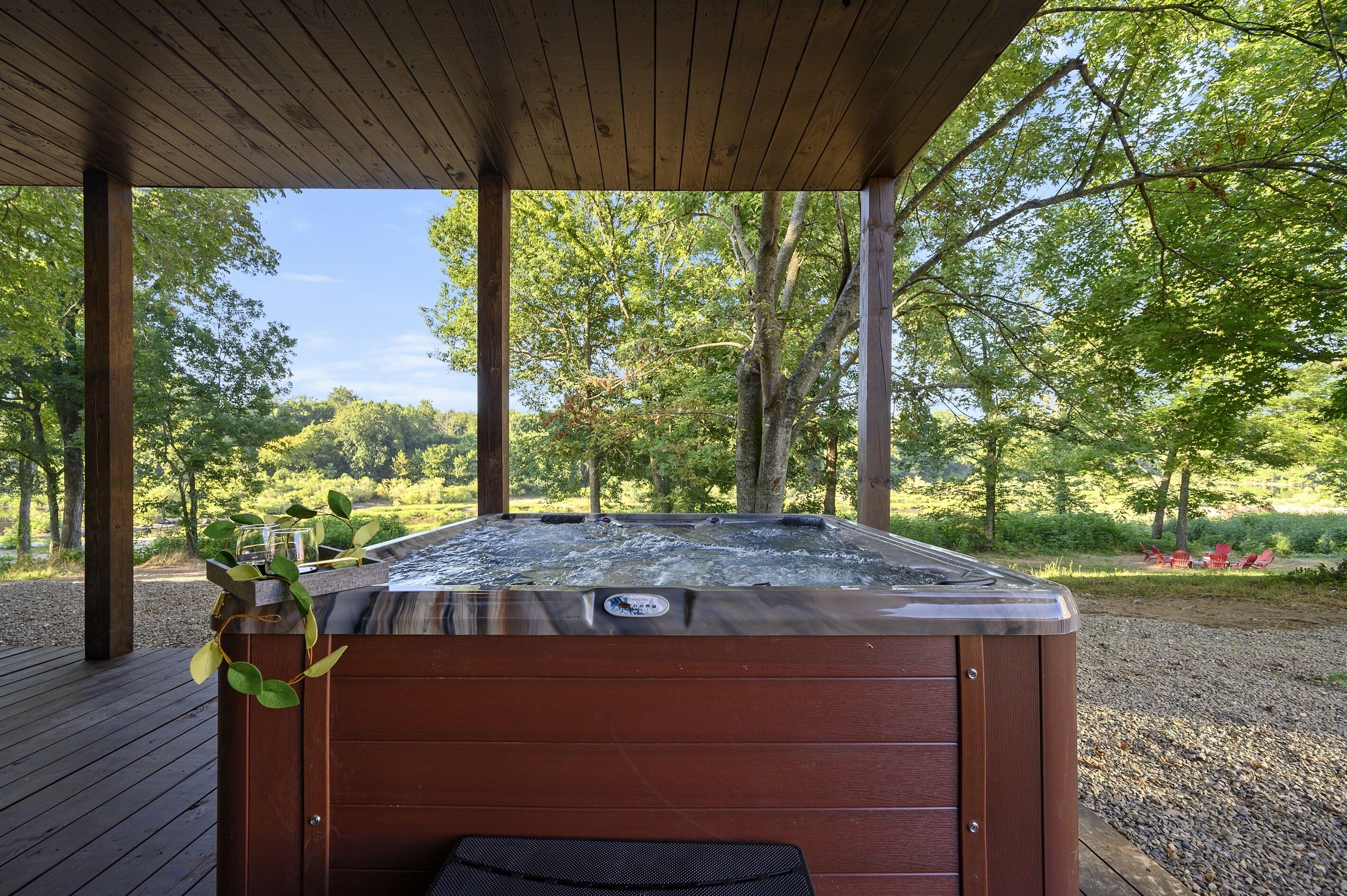 A hot tub under a wooden deck with a view of a forested area.