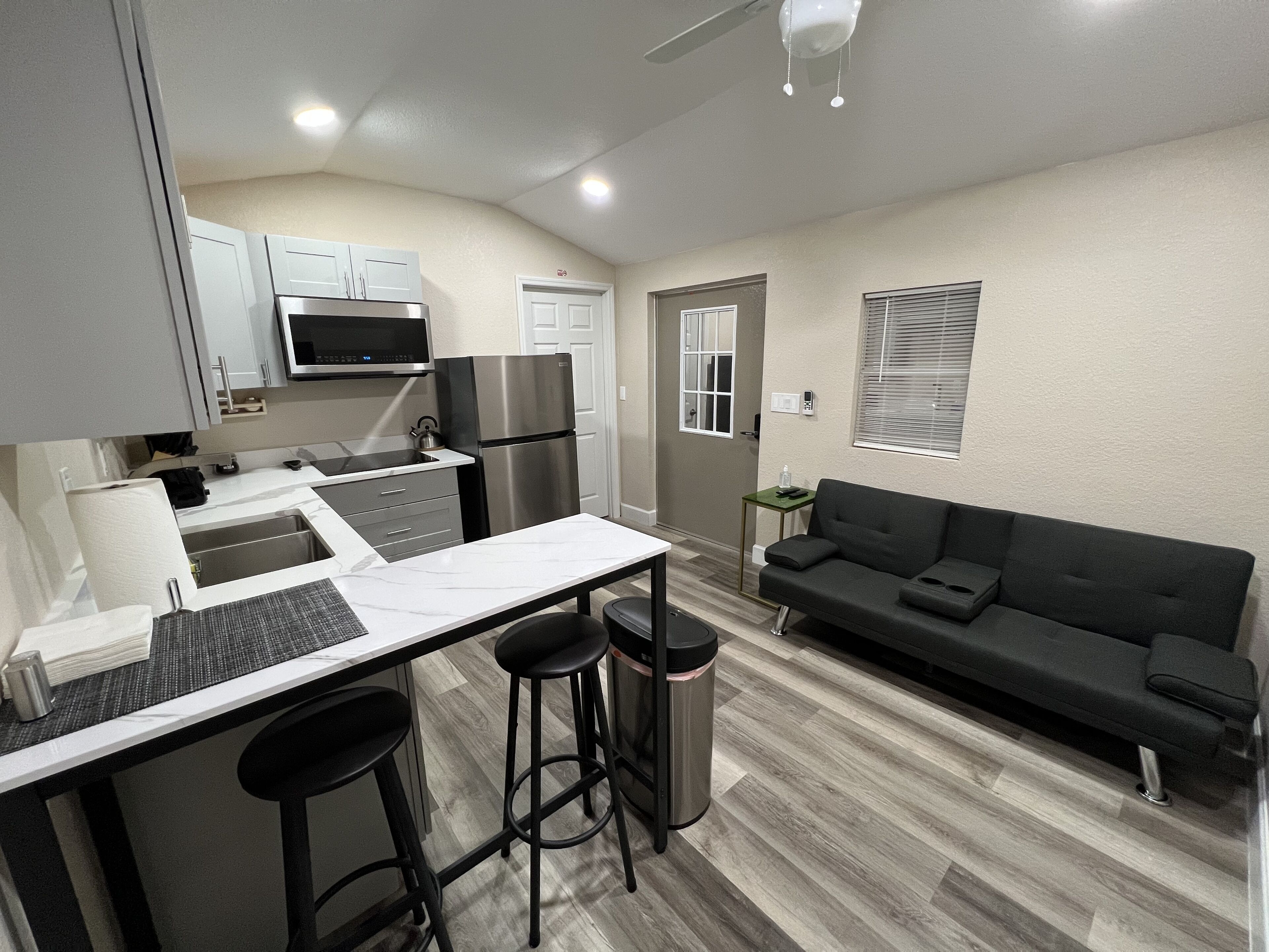 A compact kitchen with a microwave, refrigerator, and bar stools. A small dining table is also visible.