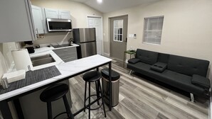 Cozinha compacta com micro-ondas, frigorífico e banquetas de bar. Uma pequena mesa de jantar também é visível.