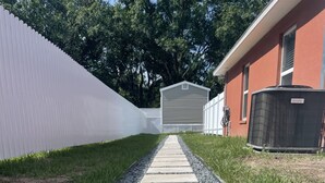 Uma trilha leva a um edifício com cerca branca e área externa coberta.