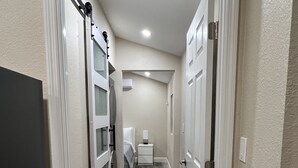 Um corredor estreito com chão de madeira, paredes brancas e uma porta no fim que dá para um banheiro.