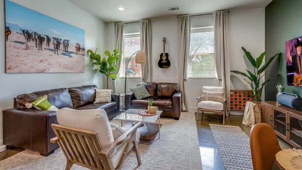 A living room with a sofa, chairs, a coffee table, a guitar, and a painting of cows.