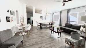 Ein modernes Wohnzimmer mit Essbereich, einem grauen Sofa und einem Deckenventilator.