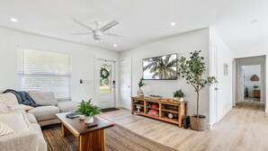 A spacious living room with a sofa, coffee table, and a wooden cabinet. - Casa Del Sol - Bike to Beach, Saltwater Pool & Private Backyard (Palm Beach Gardens)