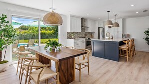 A modern kitchen with a central island, white cabinetry, and a view of a garden. - Casa Del Sol - Bike to Beach, Saltwater Pool & Private Backyard (Palm Beach Gardens)