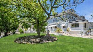 A house with a well-maintained lawn, a stone circular garden feature, and a large tree providing shade.