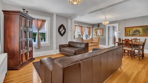 A spacious living room with a large brown leather sofa, a wooden cabinet, and a dining area with a wooden table and chairs.