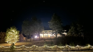 A building with a lighted facade, surrounded by trees and a fence with string lights. - Mountain Luxury and Views Galore Near Palmer Lake (Larkspur)