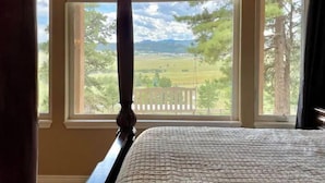 A bedroom with a four-poster bed, large windows with a view of a rural landscape, and a wooden headboard. - Mountain Luxury and Views Galore Near Palmer Lake (Larkspur)