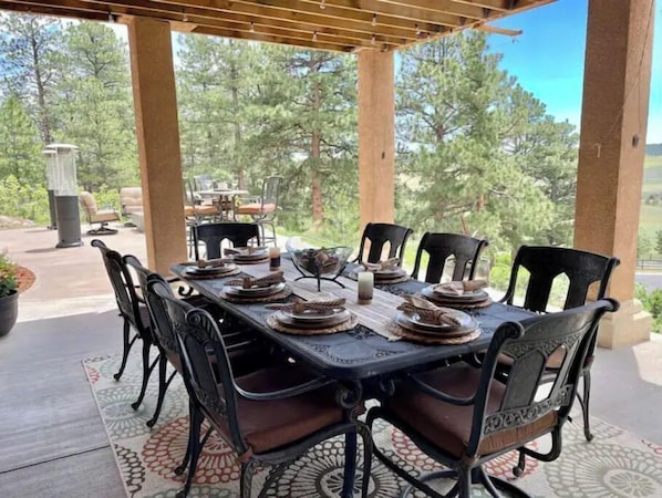 An outdoor dining area with a table set for six, surrounded by chairs, under a pergola.