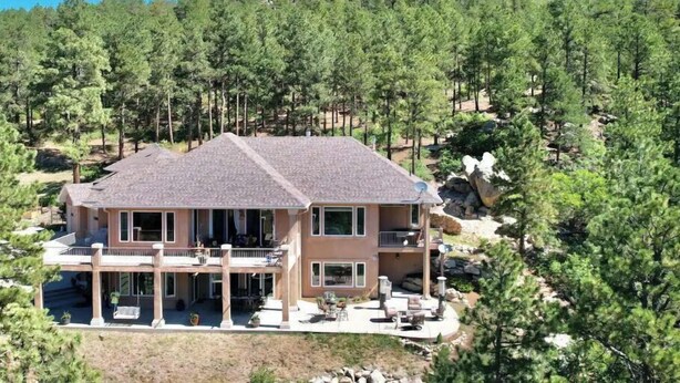 A two-story house with a balcony, surrounded by trees and a rocky hill in the background. - Mountain Luxury and Views Galore Near Palmer Lake (Larkspur)