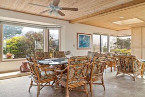 A dining area with wicker chairs, a round table, and large windows with a view of trees and a building.