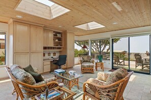 A spacious room with a high ceiling, wooden cabinets, a desk, and comfortable seating.