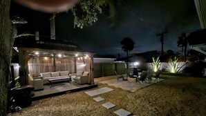 Un espacio al aire libre techado con sofá y sillones, una parrilla y un pequeño hogar para fuego.