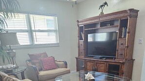 Una sala de estar con una mesa de centro de vidrio, dos sofás, un televisor sobre un mueble de madera y una alfombra estampada.