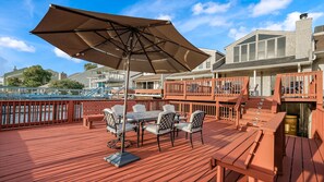 Eine Holzterrasse mit Gartenmöbeln, einem großen Sonnenschirm und Blick auf einen Hafen mit Booten.