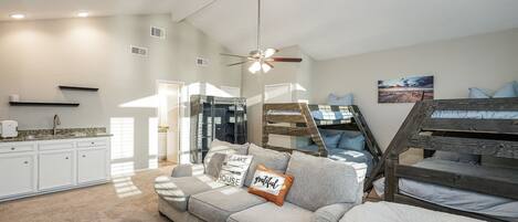 A cozy living room with a sofa, a bunk bed, a kitchen, and a dining area.