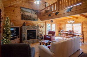 A cozy log cabin interior with a stone fireplace, a television, a Christmas tree, and a dining area with wooden furniture. - Beary Cozy Cabin in the woods near private lake! Near Lake Lure/ Chimney Rock, (Lake Lure)