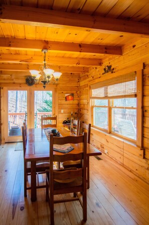 A wooden cabin interior with a dining table, chairs, a chandelier, and large windows. - Beary Cozy Cabin in the woods near private lake! Near Lake Lure/ Chimney Rock, (Lake Lure)