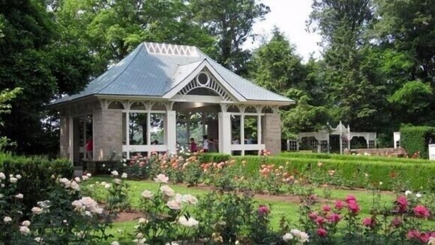 A gazebo with a peaked roof and columns, surrounded by a well-maintained garden with various flowering plants. - Cozy and completely updated The Farmhouse at Lanterman's Village (Youngstown)