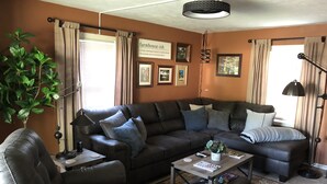 A living room with a dark brown leather sofa, a coffee table, and a large green plant. - Cozy and completely updated The Farmhouse at Lanterman's Village (Youngstown)