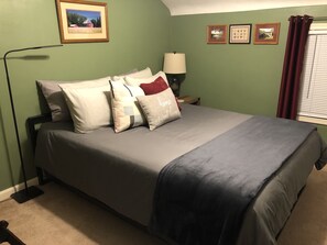 Una cama bien hecha con una colcha gris y azul, una lámpara y un cuadro en la pared.