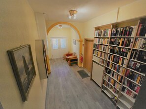 A hallway with a bookshelf, a framed picture, and a door leading to another room.