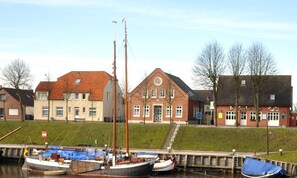 A riverside dock with boats, a building with a red roof, and a staircase leading up to a door.