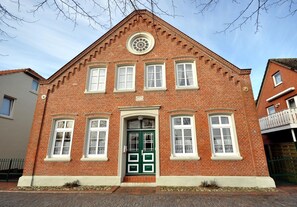 Un bâtiment en briques rouges, avec une porte verte, de nombreuses fenêtres et une fenêtre circulaire au-dessus de la porte.