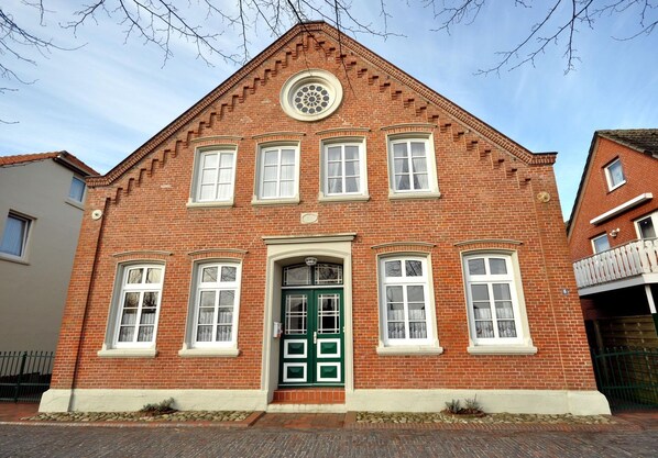 A red brick building with a green door, multiple windows, and a circular window above the door.
