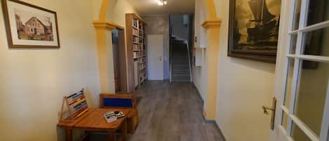 Un pasillo con una mesa y sillas de madera, una estantería y una puerta decorada con un cuadro.