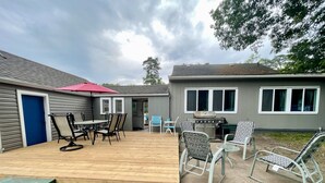Un patio trasero con una terraza de madera, una parrilla y mobiliario exterior.