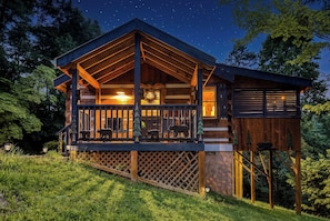 A cabin with a covered porch, a fireplace, and a deck with outdoor lighting.