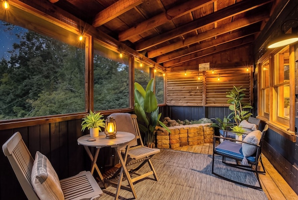 A cozy outdoor seating area with wooden furniture, string lights, and a view of the forest.
