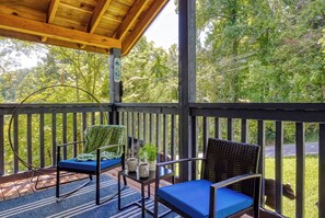 A covered outdoor seating area with two chairs and a table, surrounded by a wooden railing, overlooking a lush green landscape.