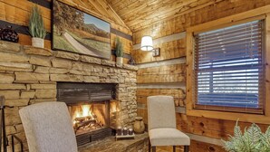 Ein gemütliches Zimmer mit Kamin aus Stein, Holzwänden und einem großen Fenster mit Jalousien.