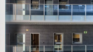 A multi-story building with a modern design, featuring balconies with glass railings, multiple windows, and emergency exit signs.