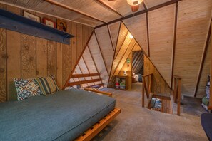 Un dormitorio acogedor en el ático con cama de altillo, vigas de madera y un pequeño rincón de lectura.