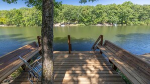 A wooden dock with benches and a tree, overlooking a calm lake with a forested shoreline.