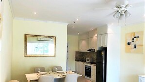 Een moderne keuken met witte kasten, een zwarte koelkast en een magnetron. Er is een eethoek met een tafel en stoelen.