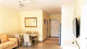 Een moderne woonkamer met een bank, eettafel, stoelen, een televisie en een deur naar een andere kamer.