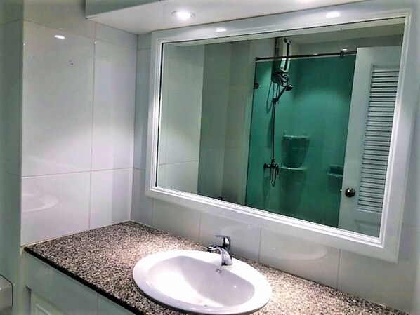 Une salle de bain avec un lavabo blanc, une cabine de douche en verre et un miroir au-dessus du lavabo.