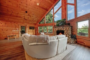 A cozy cabin interior with a stone fireplace, large windows, and a comfortable seating area. - Luxury Mountain View Cabin with Jacuzzi (Blue Ridge)